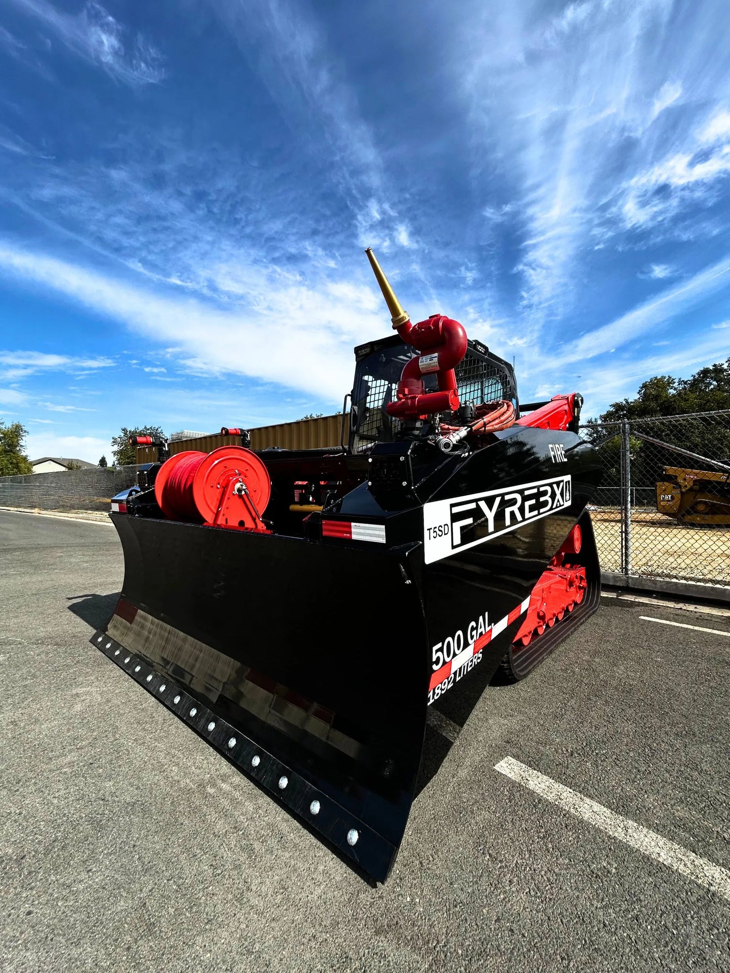 Black and red FYREBX firefighting track loader with large front blade parked outdoors on a sunny day