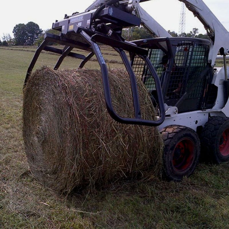 Skid Steer with Blue Diamond Bale Squeeze Attachment picking up bale.