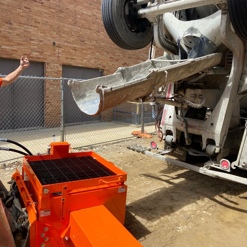 Concrete truck chute positioned over bright orange Hog Pump mixer at a construction site