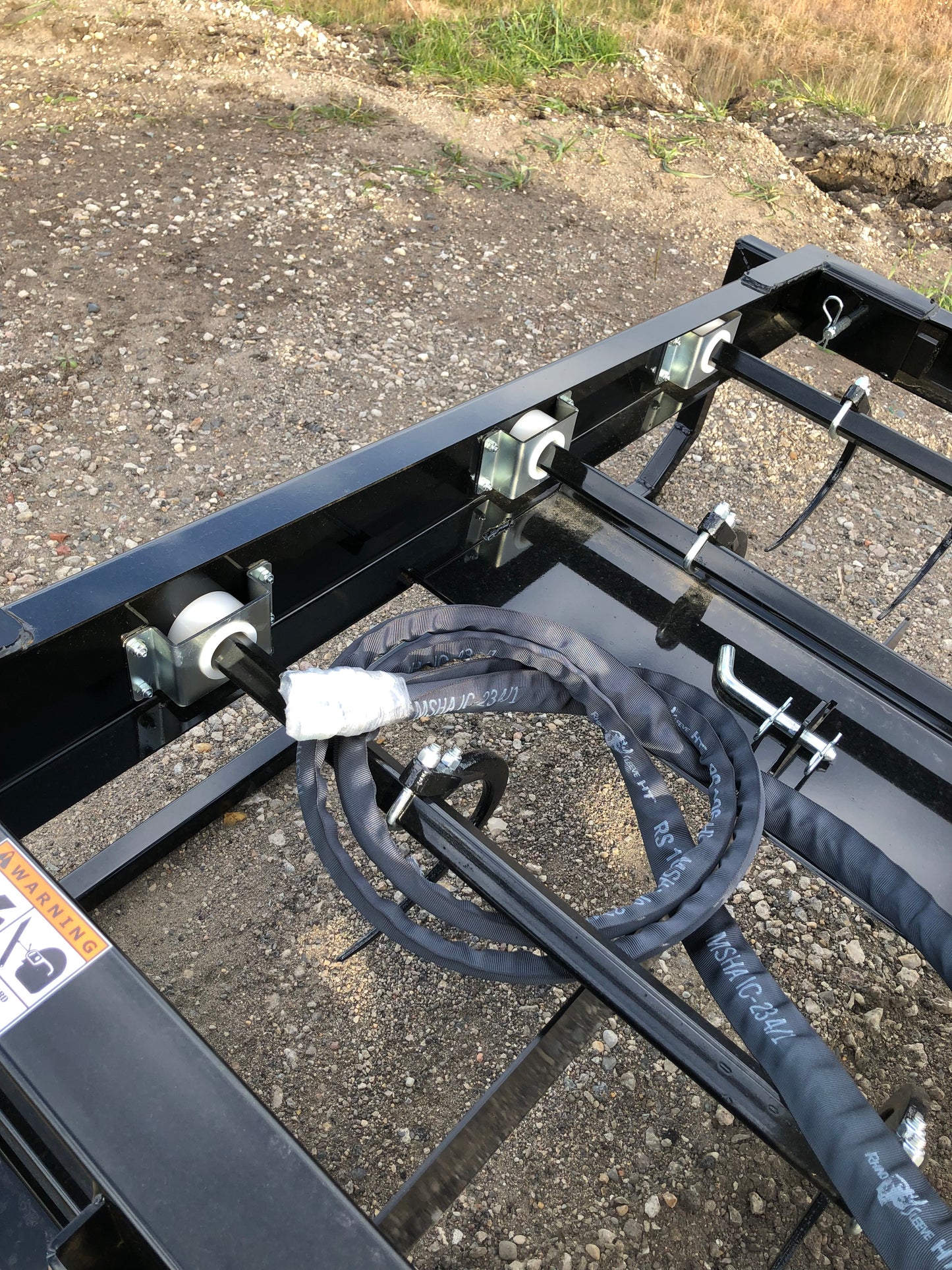 Close-up of a skid steer attachment frame with hydraulic hoses coiled and metal rollers along the top bar