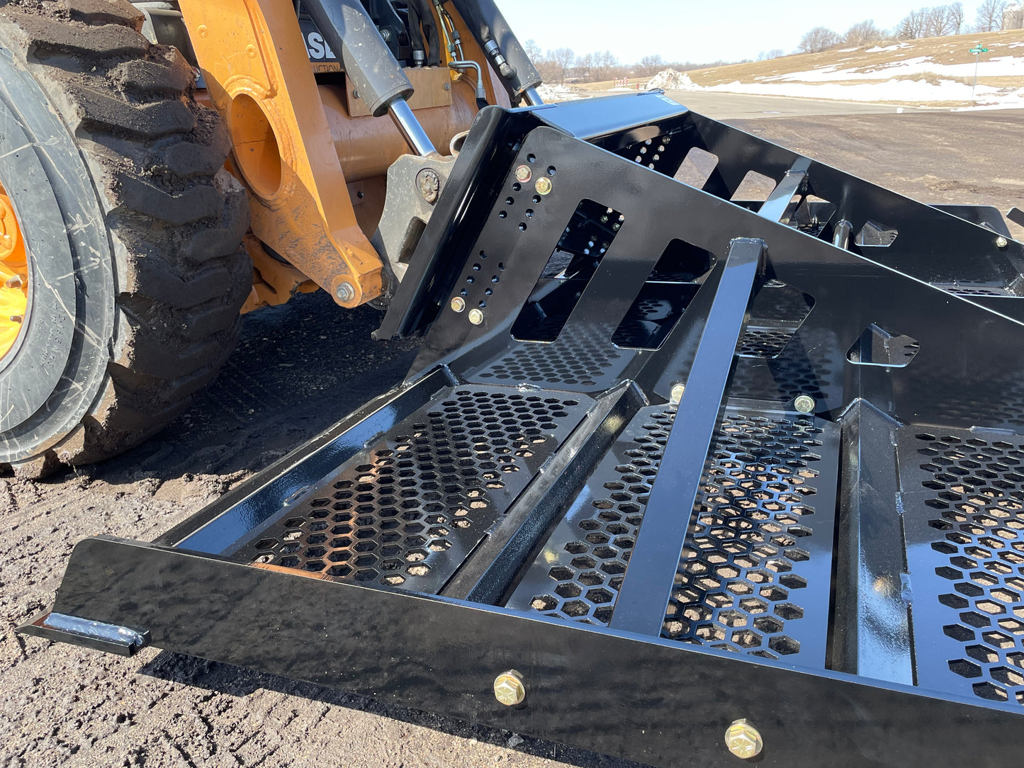 Close-up of black skid steer land leveler attachment with perforated metal floor and support beams