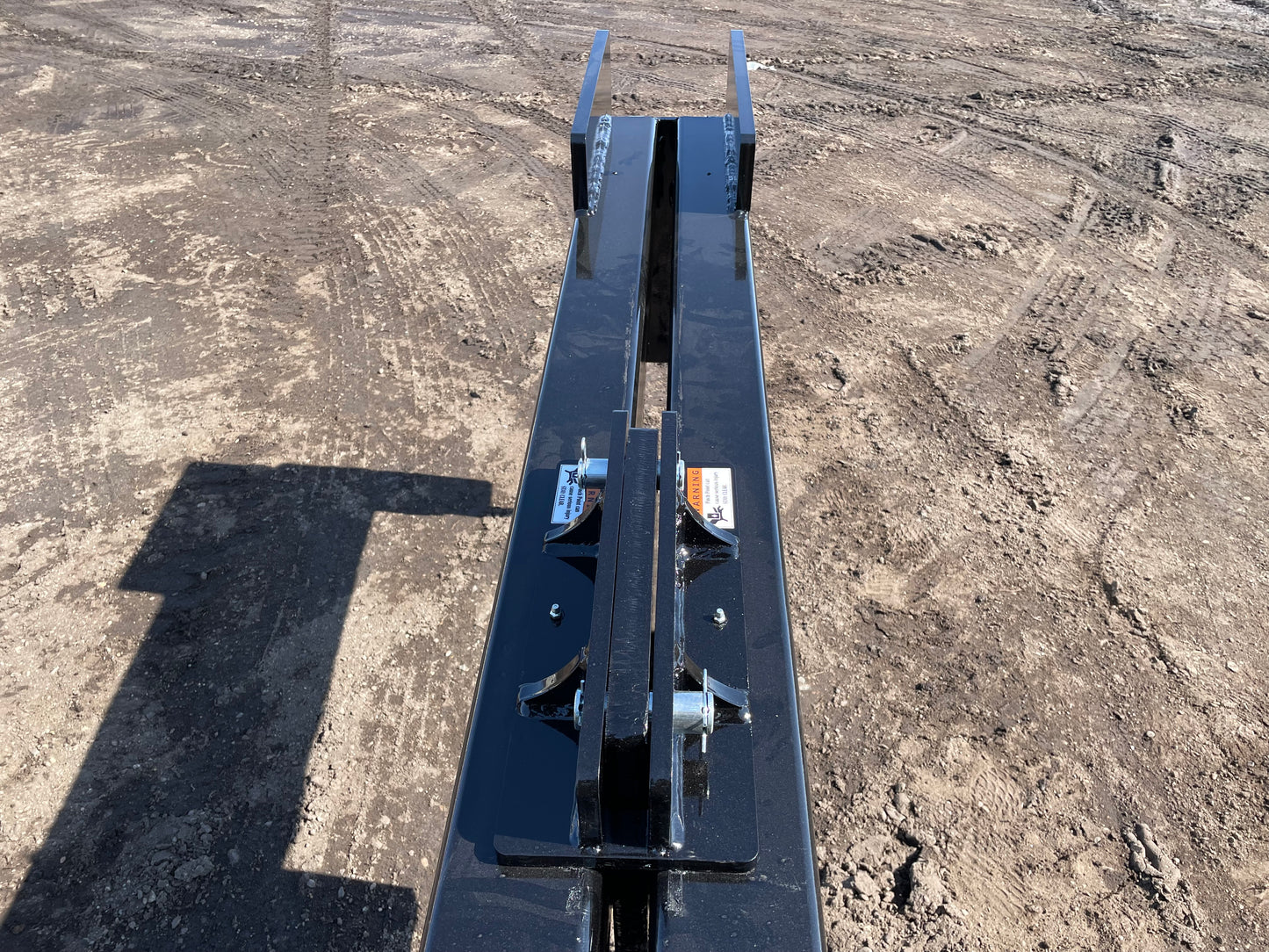 Black skid steer attachment arm facing forward on dirt worksite