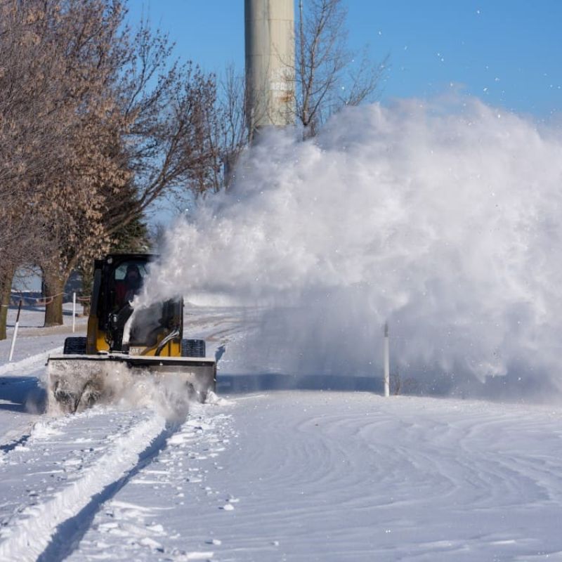 blowing the snow on the road using a skid steer with a blue diamond snow blower attachment