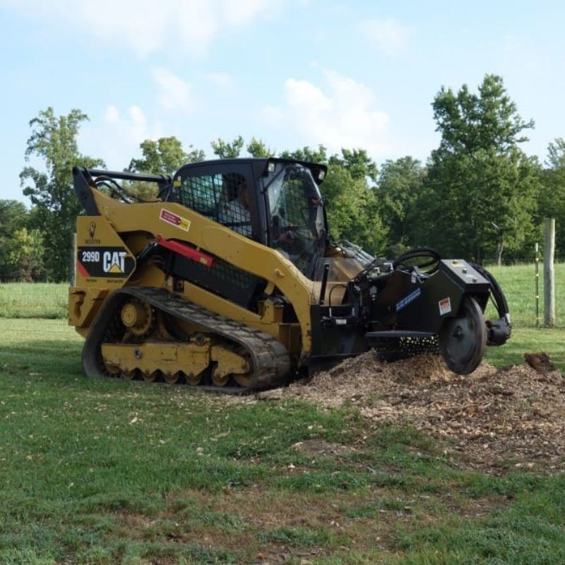 cat skid steer in the field with the blue diamond stump grinder with swing arm attachment in action