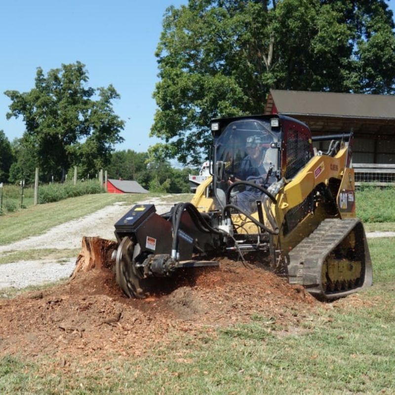case skid steer in action with the blue diamond stump grinder with swing arm attachment