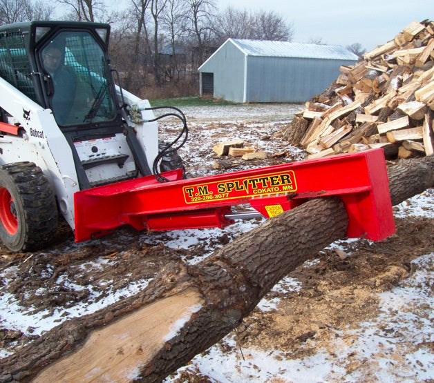 TM Manufacturing Pro Series log splitter attached to bobcat skid steer cutting a tree in half