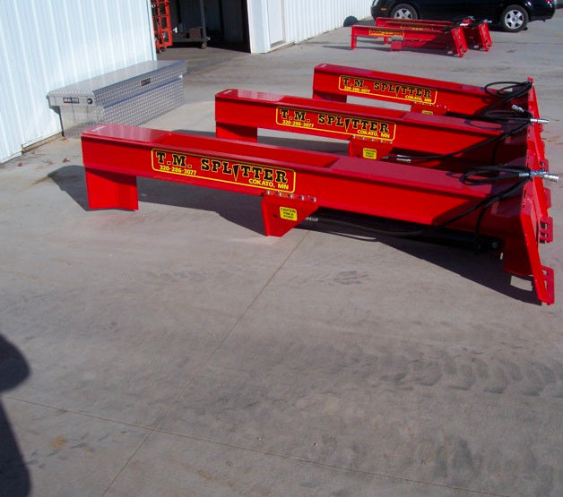 A line up of 3 TM Manufacturing Pro Series Skid Splitters Sitting on the ground