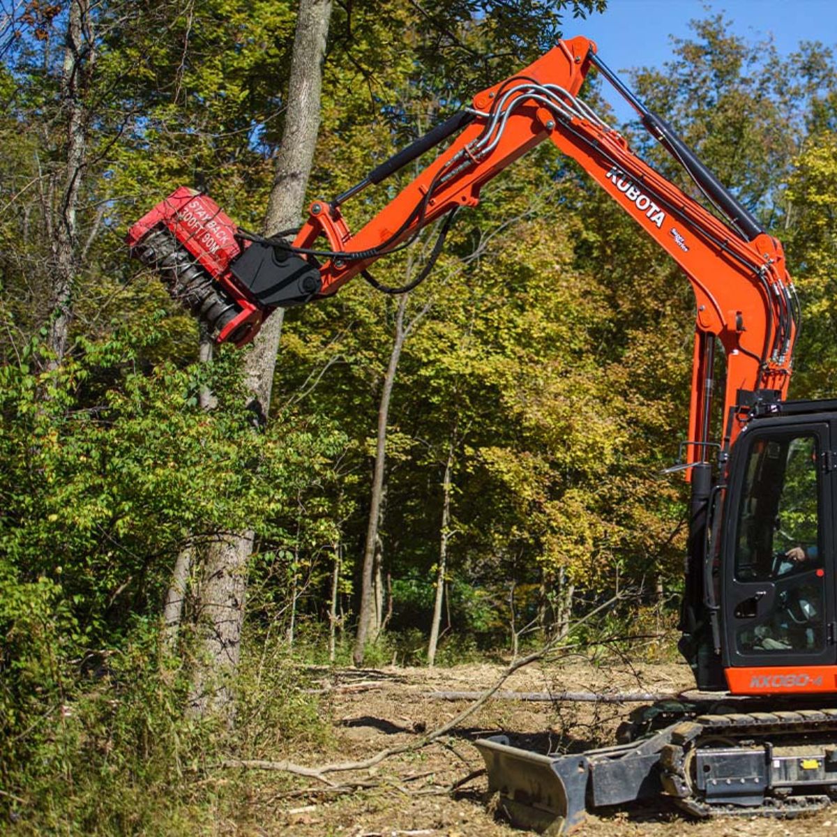 Kubota mini excavator using an FMX series drum mulcher attachment to grind a tree in a wooded area