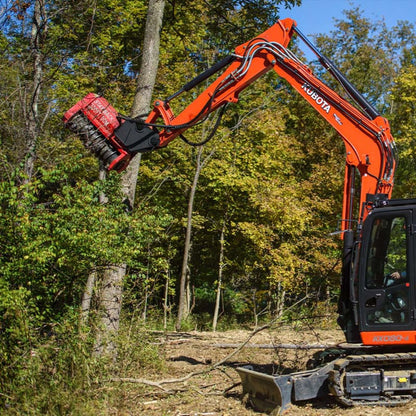 Kubota mini excavator using an FMX series drum mulcher attachment to grind a tree in a wooded area