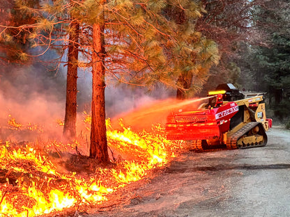 FYREBX-equipped CAT track loader spraying water on an active wildfire along a forested road