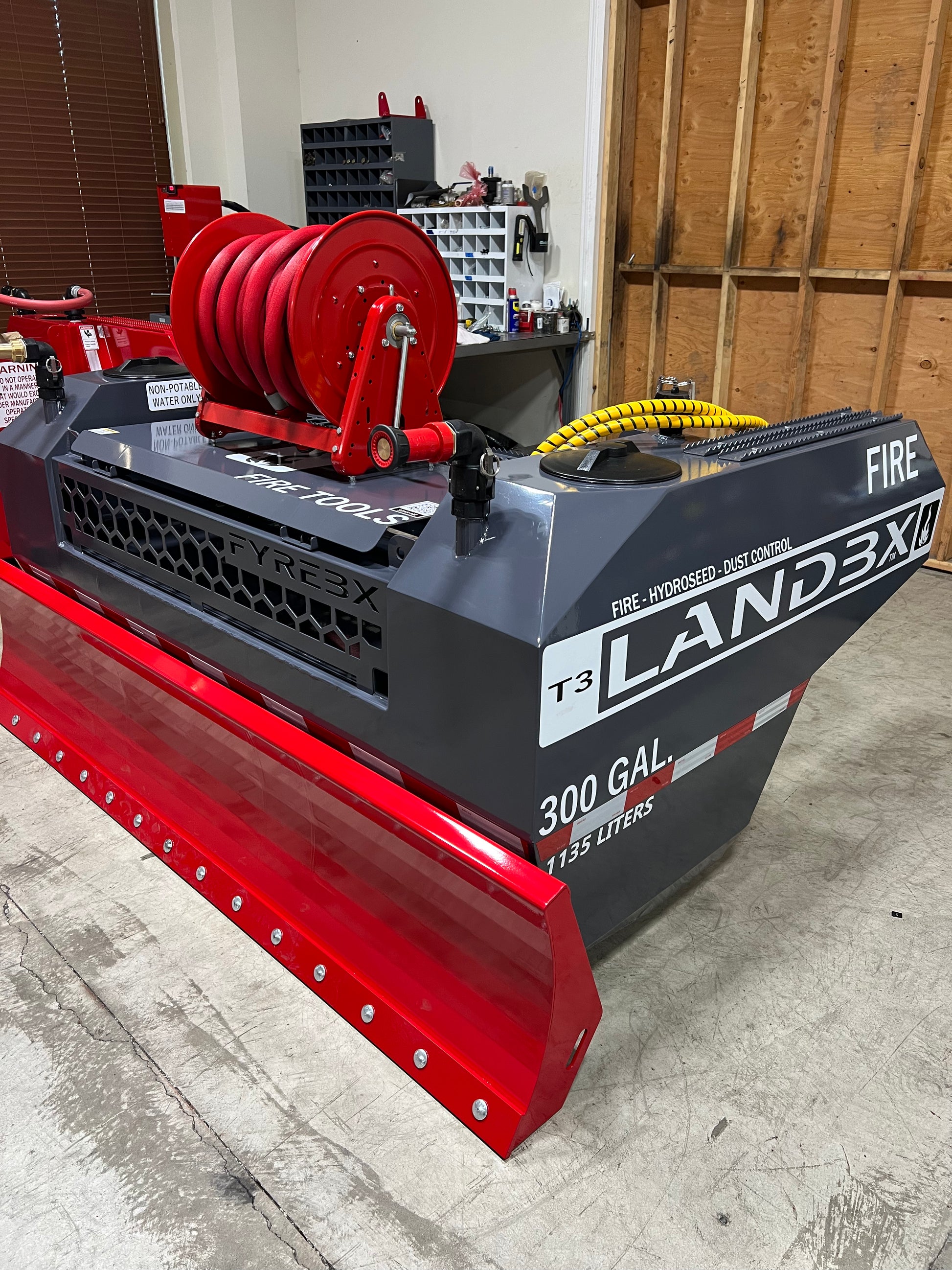 Red and gray FYREBX LANDBX T3 firefighting attachment with hose reel and 300-gallon blade