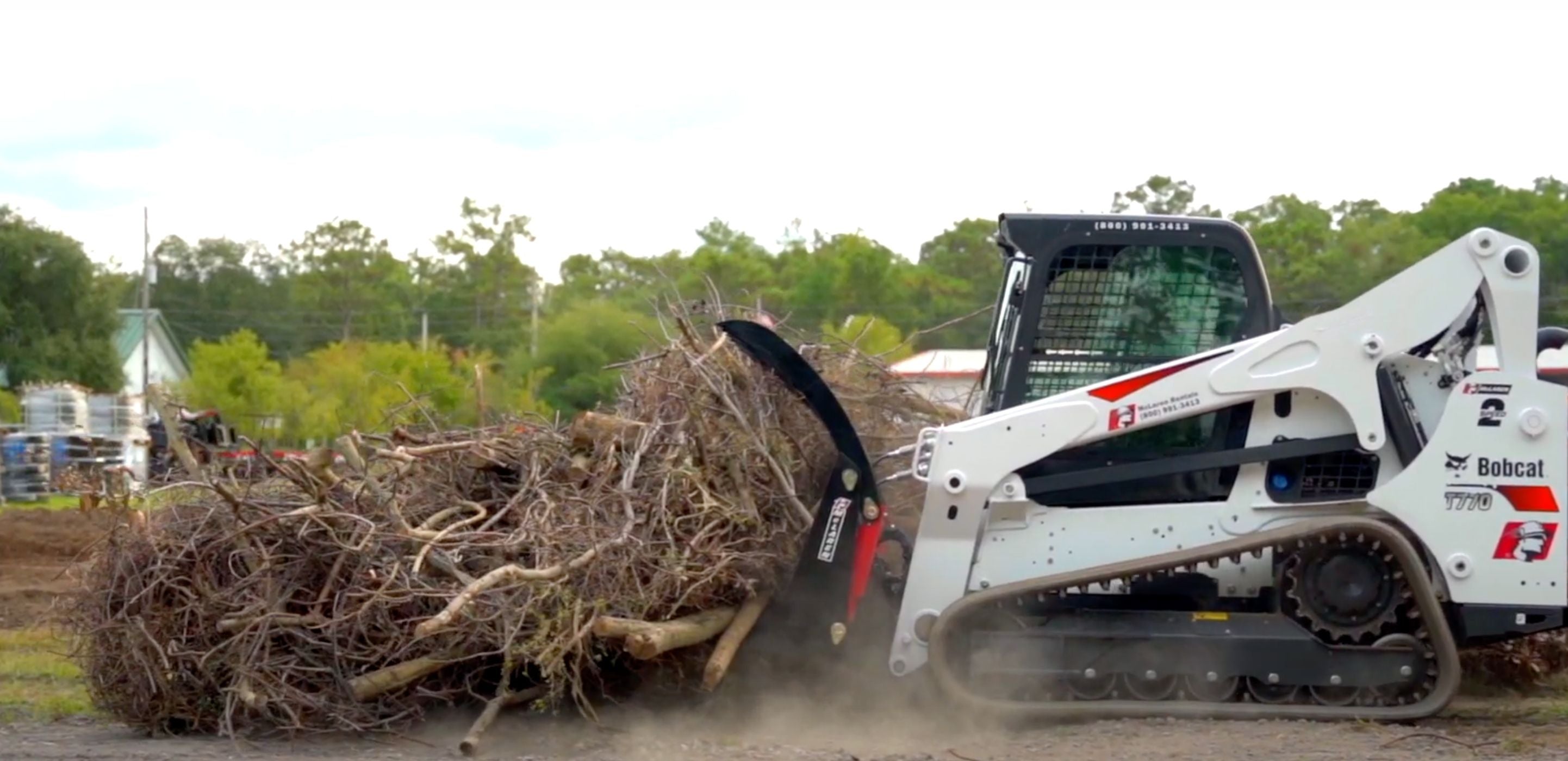 Bobcat skid steer with the grapple attachment moving woods in the garden. 