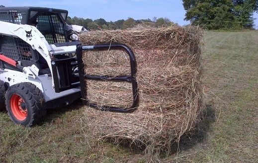 Bobcat skid steer holding a bale using the round bale grapple attachment from blue diamond