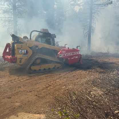 CAT skid steer with a FYREBX attachment working through smoke while controlling a small ground fire in a forested area