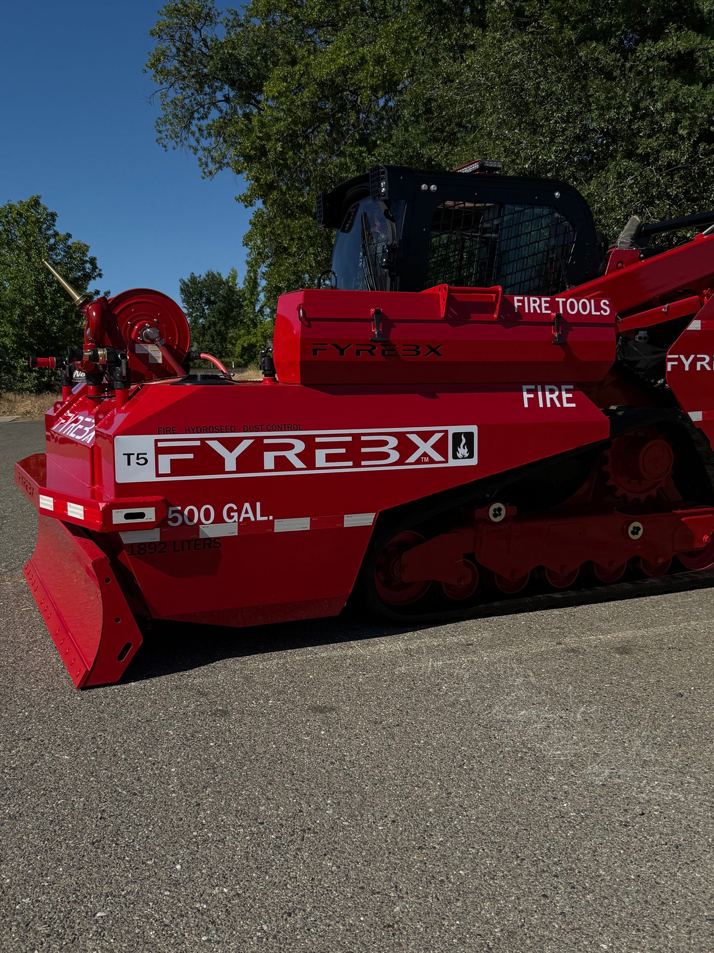Side view of a red FYREBX T5 500-gallon firefighting attachment mounted on a track loader outdoors