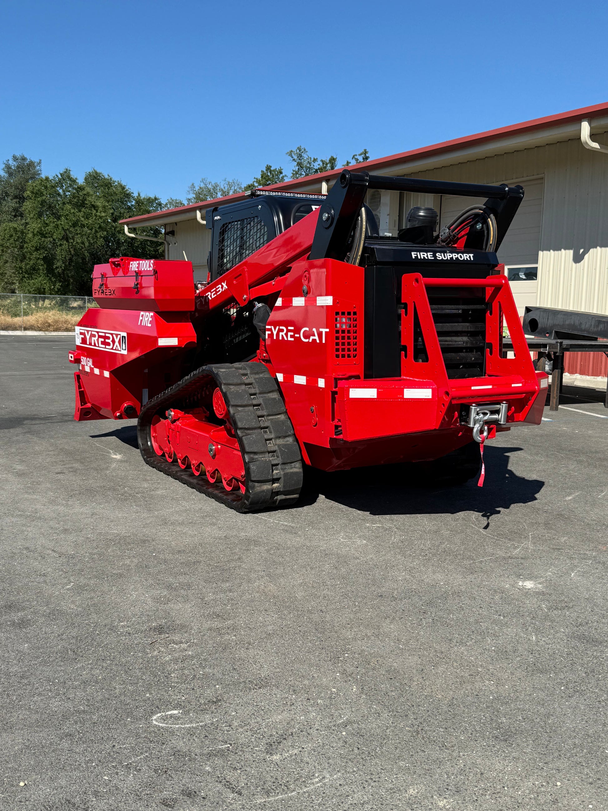 Rear view of a bright red FYRE-CAT firefighting track loader parked outside a building on a sunny day