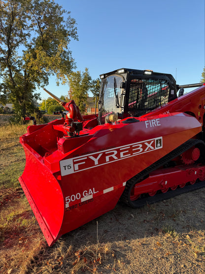 Red FYREBX T5 firefighting track loader with a 500-gallon blade attachment parked on dry grass at sunset