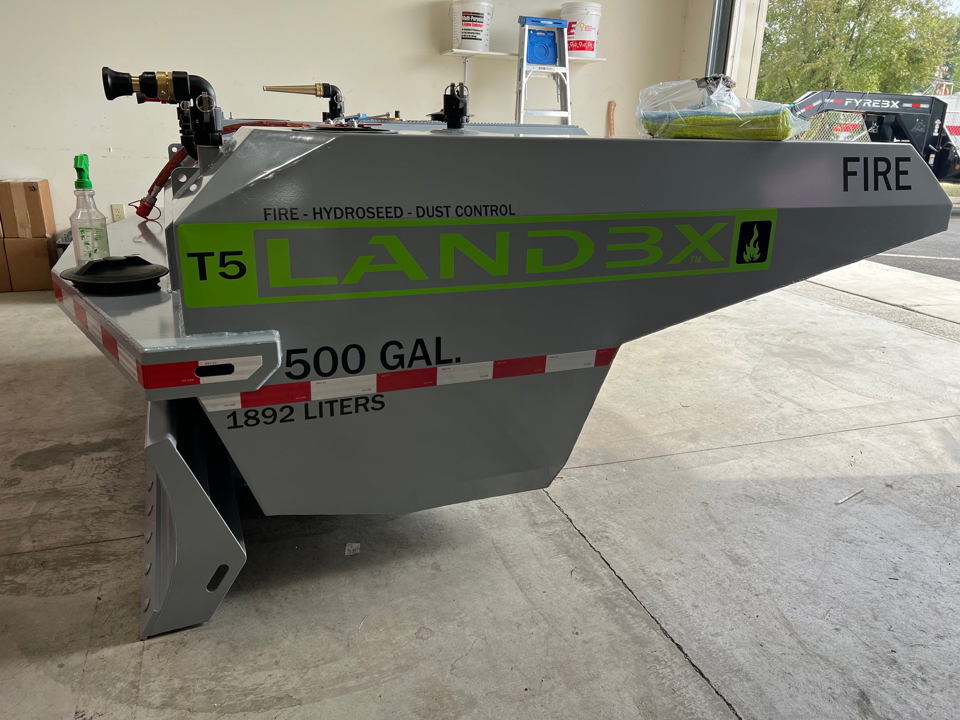 Gray FYREBX LANDBX T5 500-gallon attachment with green lettering sitting inside a garage near tools and equipment