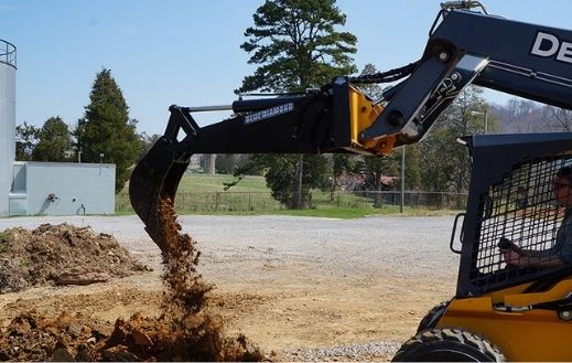 Skid steer using the Blue Diamond backhoe attachment removing dirt