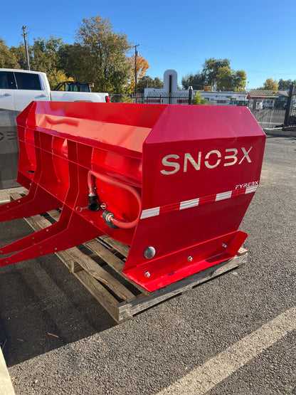 Red SNOBX FYREBX attachment with hydraulic lines, displayed on a pallet in an outdoor parking area