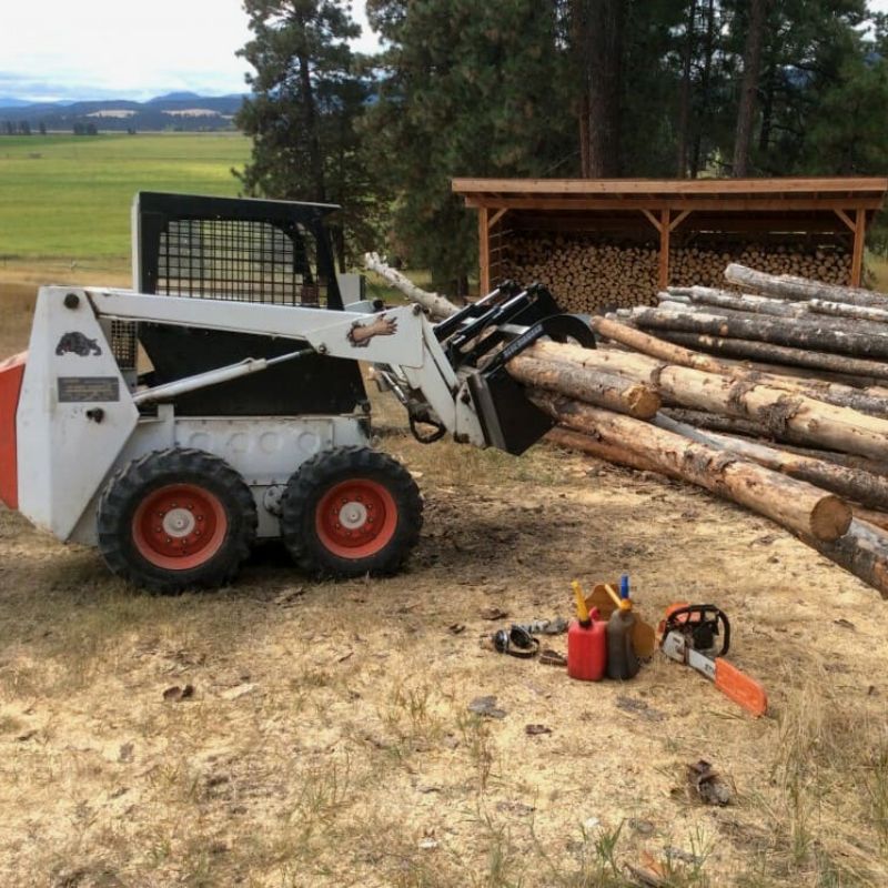 Blue diamond Light duty grapple bucket attached to bobcat skid steer moving logs into a large pile