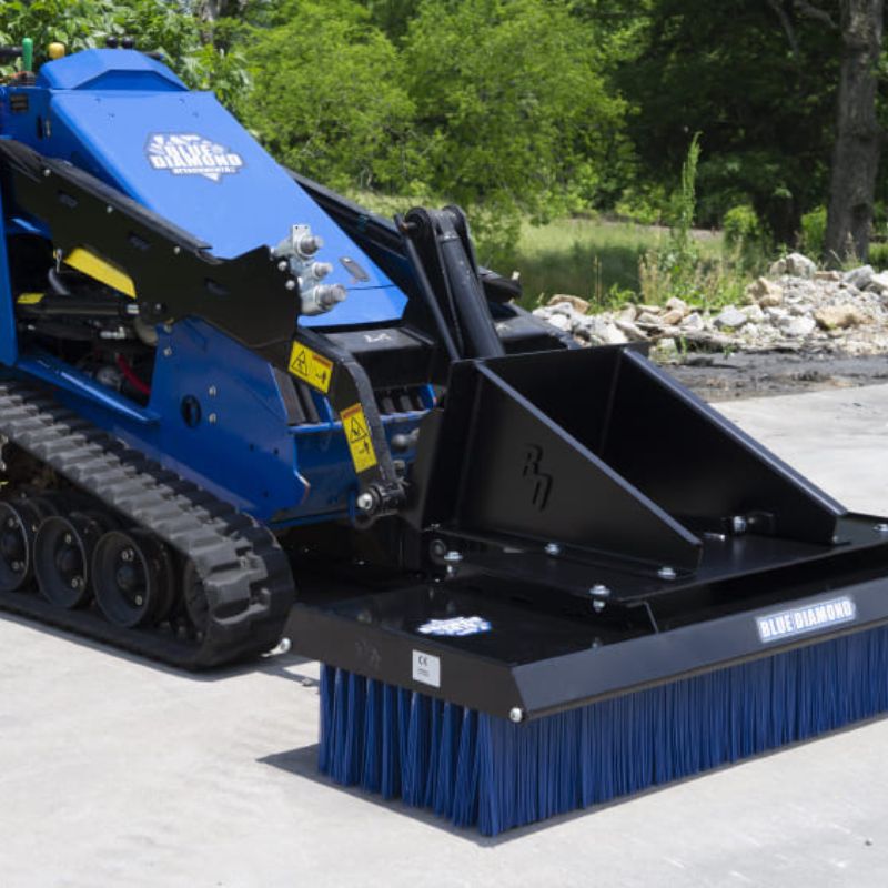 skid steer with blue diamond push broom attachment in action