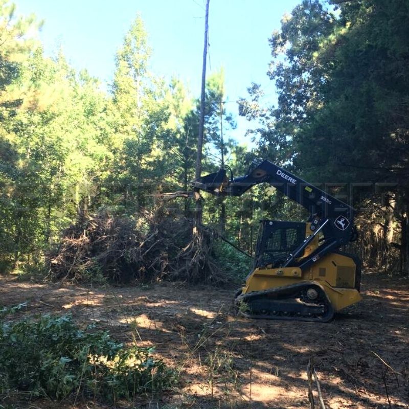 john deere skid steer with the blue diamond tree puller attachment in action pulling tree with roots
